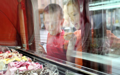 Zwei kinder schauen durch eine Scheibe auf Behälter mit Eiscreme