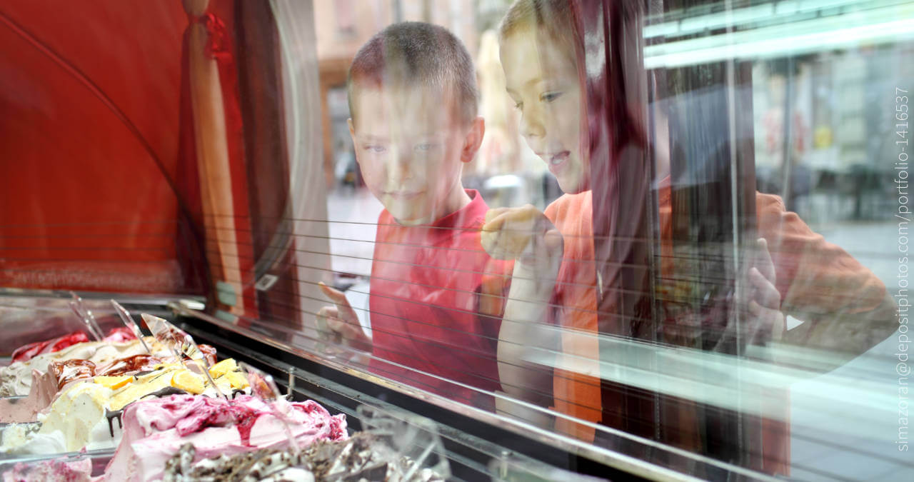 Zwei kinder schauen durch eine Scheibe auf Behälter mit Eiscreme